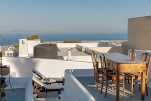 Terraço no telhado com mesa e cadeiras de madeira, uma poltrona de descanso e vista para o mar e montanhas ao longe.
