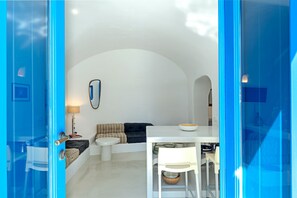 Quarto com um sofá branco, uma mesa redonda pequena, um abajur e um espelho na parede.