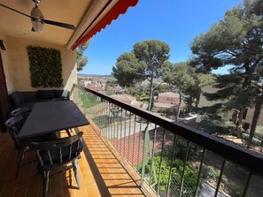 Ein Balkon mit Tisch und Stühlen, einem Deckenventilator und Blick auf eine Stadt mit Bäumen und Gebäuden.