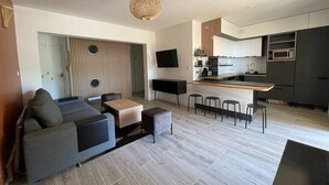 Ein modernes Wohnzimmer mit grauem Sofa, einer Wand mit Holzverkleidung und einer Küchenzeile inklusive Mikrowelle und Fernseher.