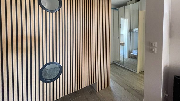 Ein modernes Interieur mit vertikalen Holzleisten, zwei runden Spiegeln und Blick in einen Raum mit Glastür.