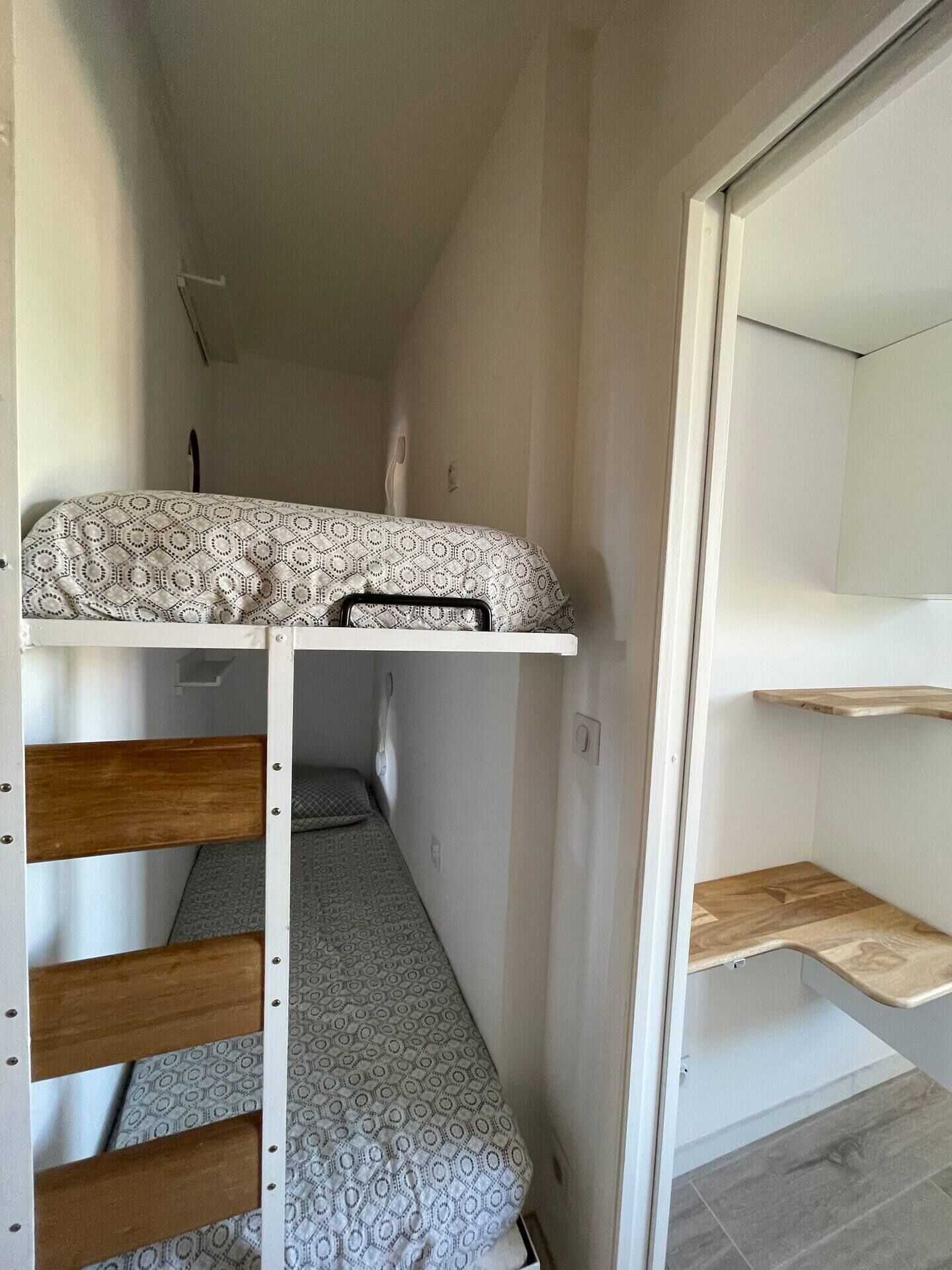 Un lit superposé avec une literie à motifs, une tête de lit en bois et une petite table de chevet.