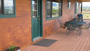 Een overdekt houten terras met een tafel en stoelen, een groene deur en potplanten.
