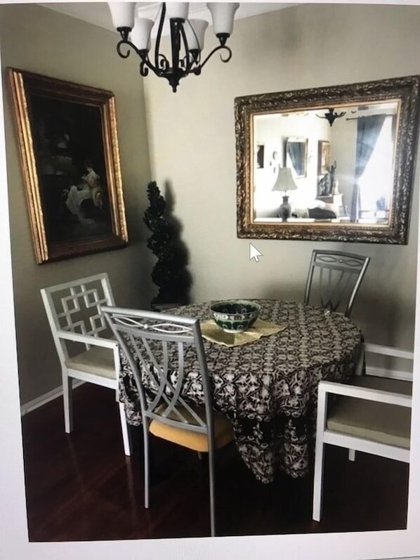 A dining area with a round table, white chairs, a chandelier, a mirror, and a framed picture on the wall.