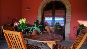 Un conjunto de mesa y sillas de madera al aire libre, con un muro de ladrillo y una ventana al fondo.