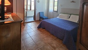 Un dormitorio con techo de madera, una cama con manta azul, un escritorio con lámpara y una silla.