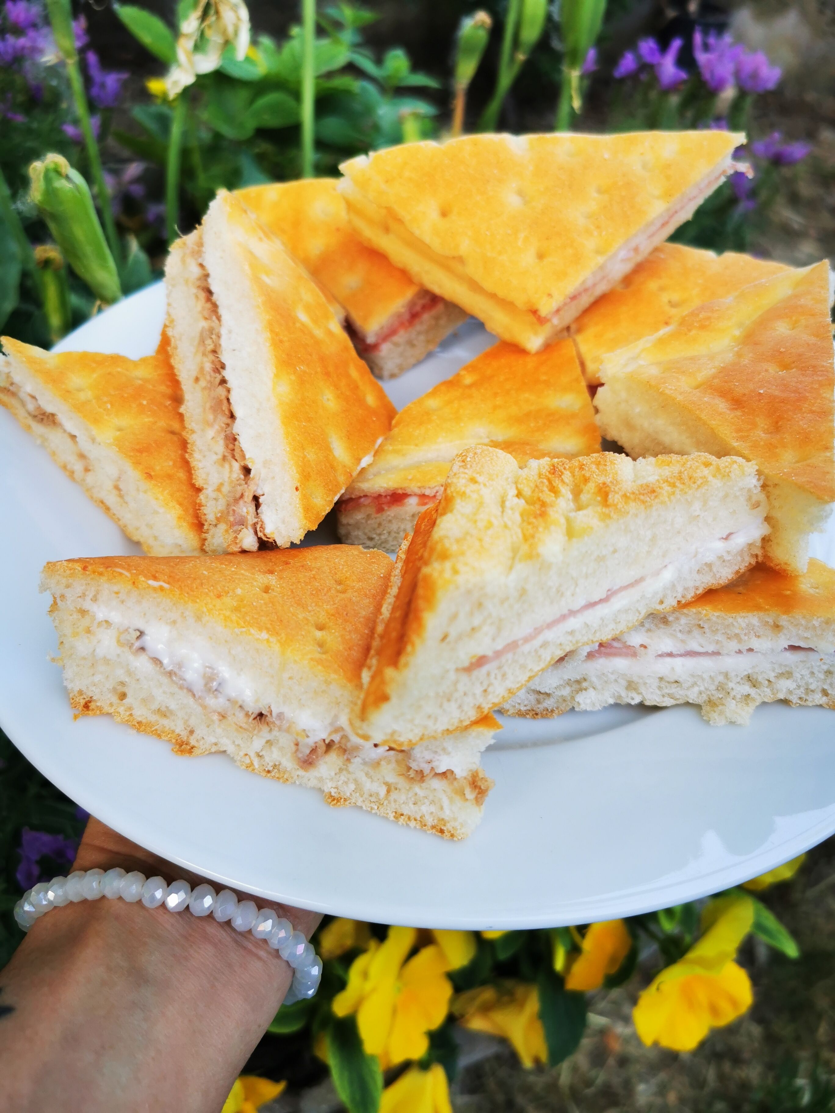A plate of triangular sandwiches with visible fillings, held by a person wearing a bracelet.