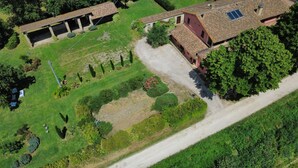 Vista aérea de una propiedad con un patio amplio y abierto, un área de estar cubierta al aire libre y un edificio con tejado de baldosas.