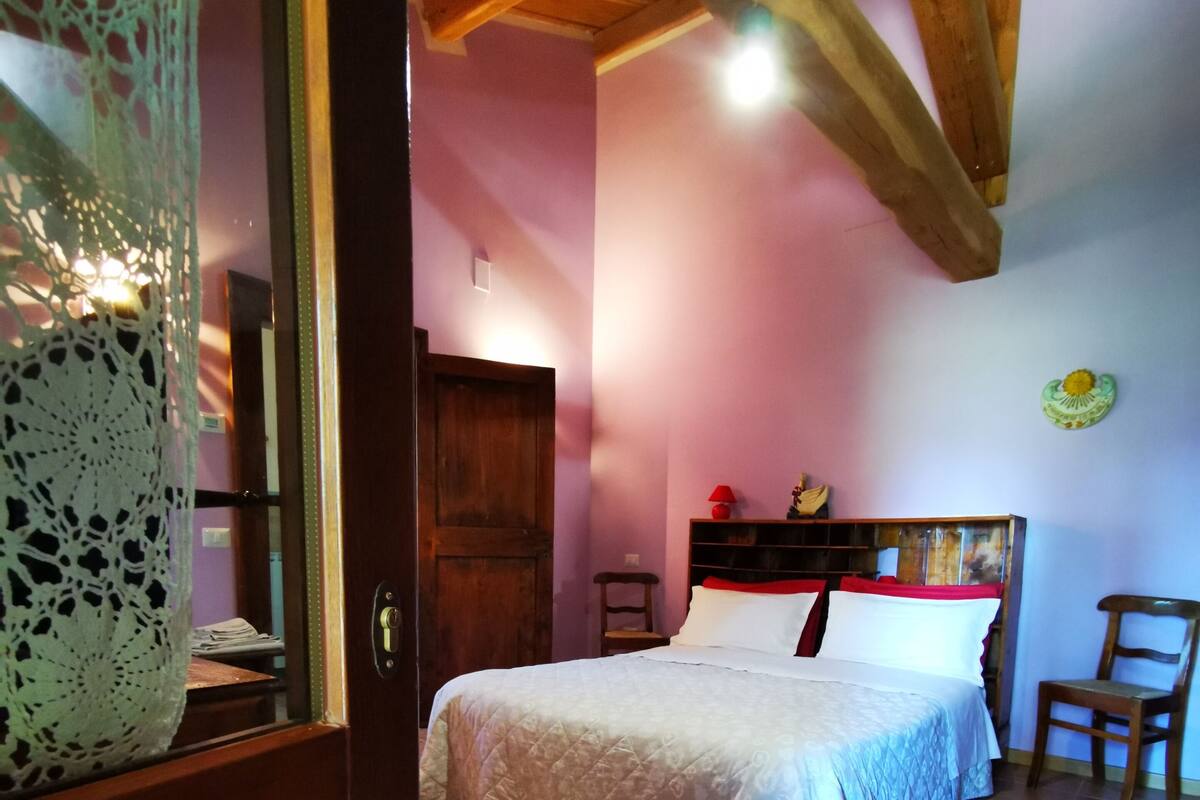 A bedroom with a bed, a chair, a wooden door, and a tiled floor.