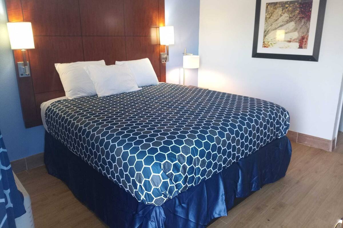 A hotel room with a large bed, two bedside lamps, a wooden headboard, and a framed picture on the wall.