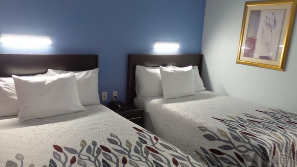 A hotel room with two beds, each with white bedding and a patterned duvet cover. There are bedside tables with lamps and a framed picture on the wall. - Budget Inn Alexandria (Alexandria)