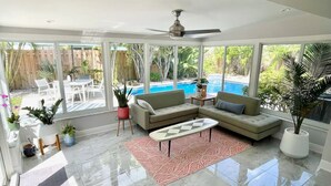 Un vaste salon doté d’une grande porte-fenêtre donnant sur une piscine, d’un ventilateur de plafond et de diverses plantes en pot.