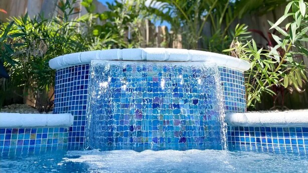 Un bain à remous aux carreaux de mosaïque, situé dans un espace piscine entouré de verdure.