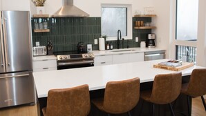 Eine moderne Küche mit einem Edelstahl-Kühlschrank, einer großen Insel mit braunen Stühlen, einem Gasherd und einer grünen Fliesenspiegel.