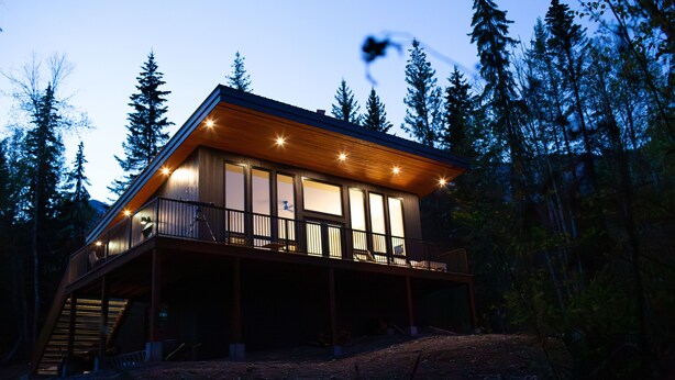 Eine Holzhütte mit großen Fenstern und einem Balkon, umgeben von Bäumen.