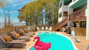 A swimming pool with a pink flamingo float, lounge chairs, and a view of the ocean. - Waterfront, Stunning Views + Pool + Kayaks! Pet friendly! (Corolla)