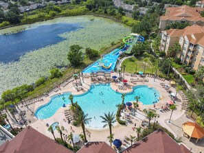 Une grande piscine extérieure divisée en plusieurs zones, entourée d’espaces de détente, de palmiers et d’un toboggan aquatique.