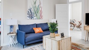 A modern living room with a blue sofa, a coffee table, and a large plant. - Charming Coastal Getaway: Explore and Relax in our 2 Bedroom Downtown Rental (Colonial Beach)