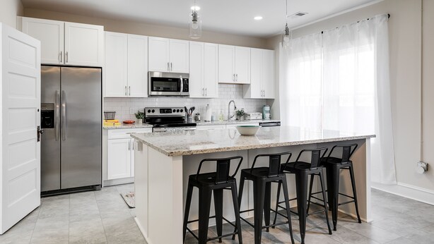 A modern kitchen with white cabinets, stainless steel appliances, a granite countertop, and black bar stools. - Charming Coastal Getaway: Explore and Relax in our 2 Bedroom Downtown Rental (Colonial Beach)