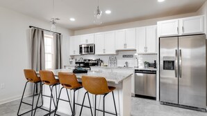 A modern kitchen with white cabinets, stainless steel appliances, and a central island with bar stools.
