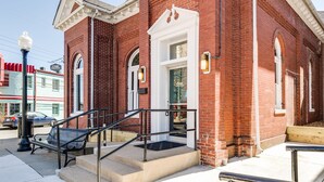 A red brick building with a white door, steps, and a bench outside.
