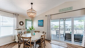 A dining area with a round table, wooden chairs, a chandelier, and a view of the outdoors through large sliding glass doors.