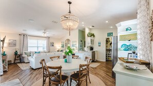 A modern kitchen with white cabinets, a dining area with a round table and chairs, and a chandelier.