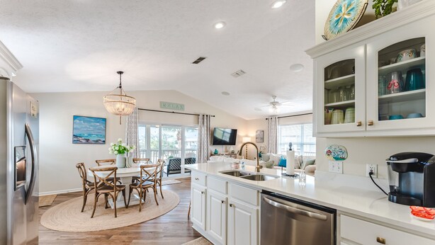 A modern kitchen with white cabinetry, a stainless steel dishwasher, and a dining area with a round table and chairs.