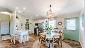 A spacious kitchen with a central island, wooden chairs, and a chandelier.