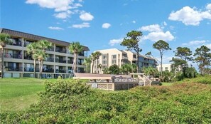 Hotel features a modern design with a flat roof and balconies on each floor, surrounded by lush greenery.