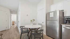 A compact kitchen with a stainless steel refrigerator, a white dining table with four chairs, and a small potted plant. - Stunning NEW / 2BR/Walk to Beach/Sleeps 5/Bunk (Panama City)