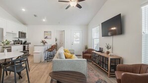 A modern living room with a grey sofa, a brown leather chair, and a dining area with a white table and chairs. - Stunning NEW / 2BR/Walk to Beach/Sleeps 5/Bunk (Panama City)