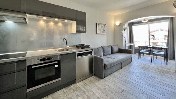 A modern kitchen with stainless steel appliances, a grey sofa, and a dining area with a table and chairs. - Bright 26 m² with pool in Frejus (Fréjus)