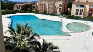 A swimming pool with a curved design, surrounded by a tiled deck and palm trees. - Bright 26 m² with pool in Frejus (Fréjus)