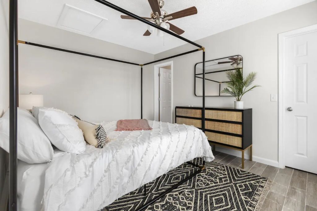 Une chambre à coucher avec un lit à baldaquin, un ventilateur de plafond, une table de chevet avec une lampe, un miroir et une plante.