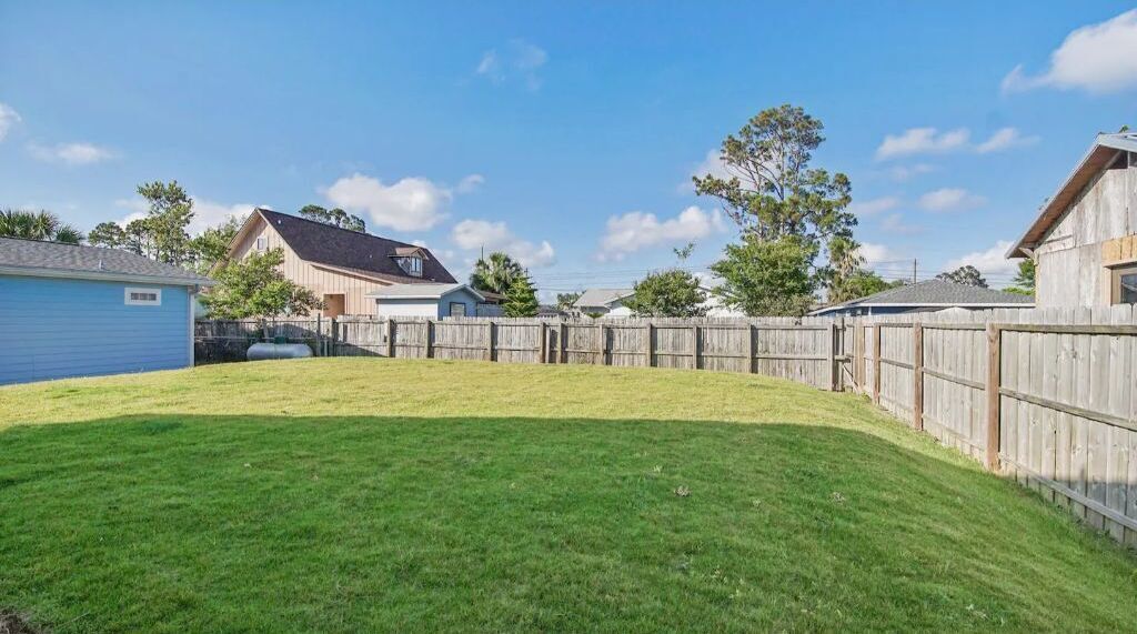 A backyard with a wooden fence, a blue shed, and a house with a sloped roof.