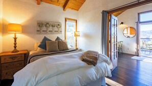 Une chambre à coucher avec un grand lit, deux lampes de chevet, une table de nuit en bois, une fenêtre et une vue sur l’extérieur.