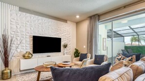 Una sala de estar moderna con televisor de pantalla plana, sofá de cuero y puerta de vidrio que da a un espacio exterior.