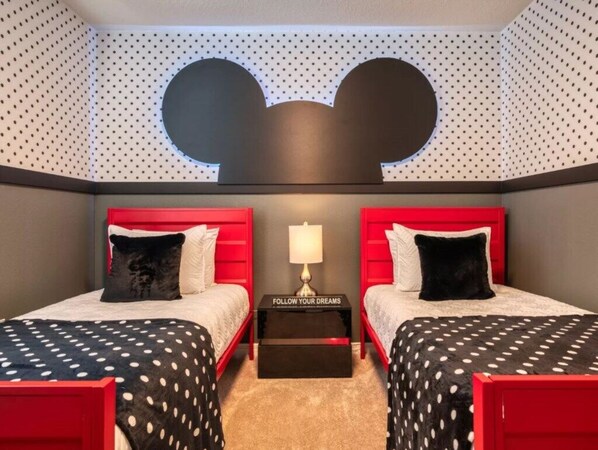 A room with two beds, a wall-mounted Mickey Mouse design, and a nightstand with a lamp.