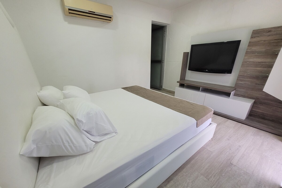 A modern hotel room with a large bed, a flat-screen TV mounted on the wall, and a wooden accent wall.