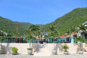 A hotel with outdoor seating, palm trees, and a mountainous backdrop. - Hotel Kaamu Taganga (Santa Marta)
