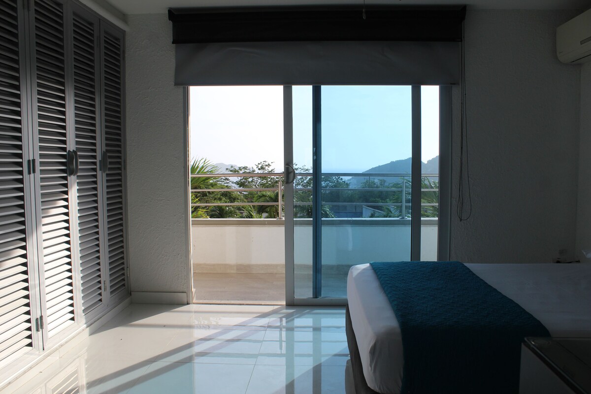 A bedroom with a bed, a sliding glass door leading to a balcony, and a view of the outdoors.
