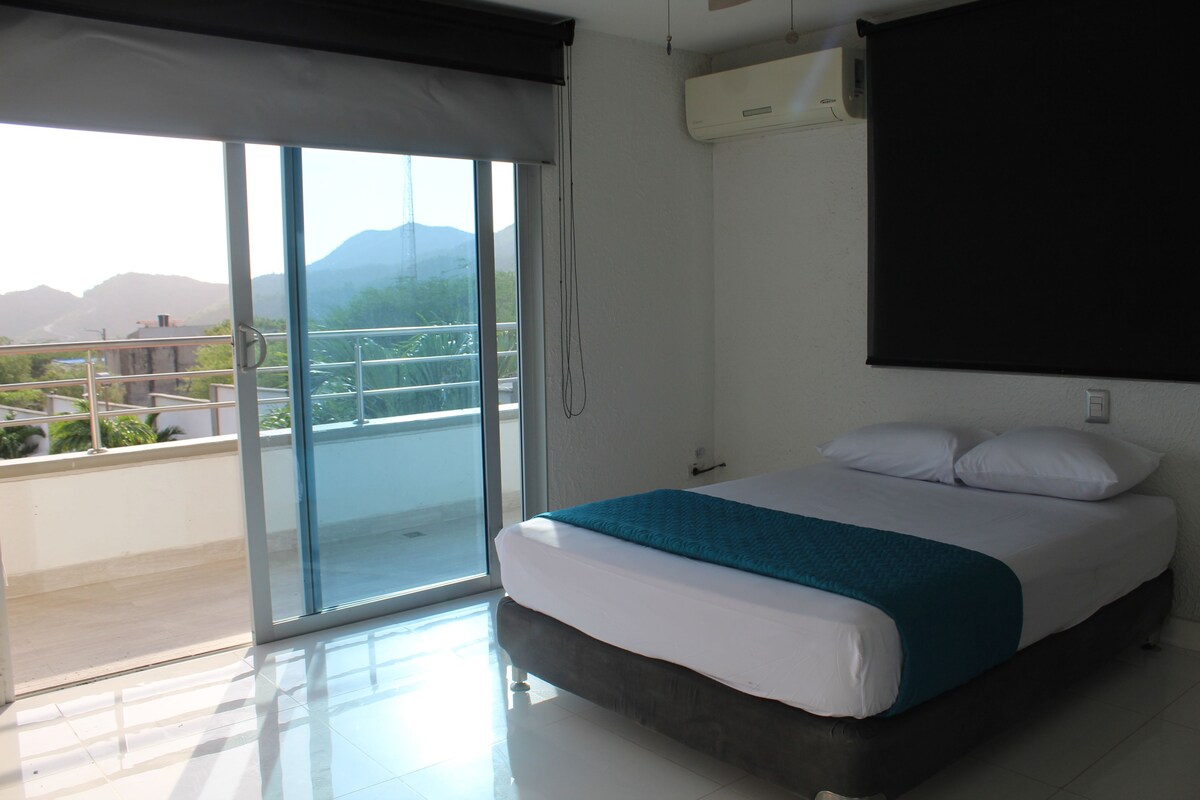 A bedroom with a bed, a view through a sliding glass door, and an air conditioning unit on the wall.