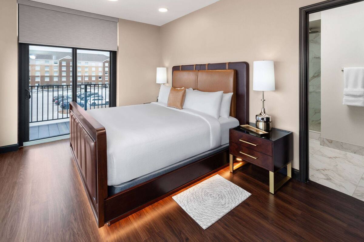 Een moderne hotelkamer met een groot bed, een nachtkastje, een lamp en uitzicht buiten via een schuifdeur.