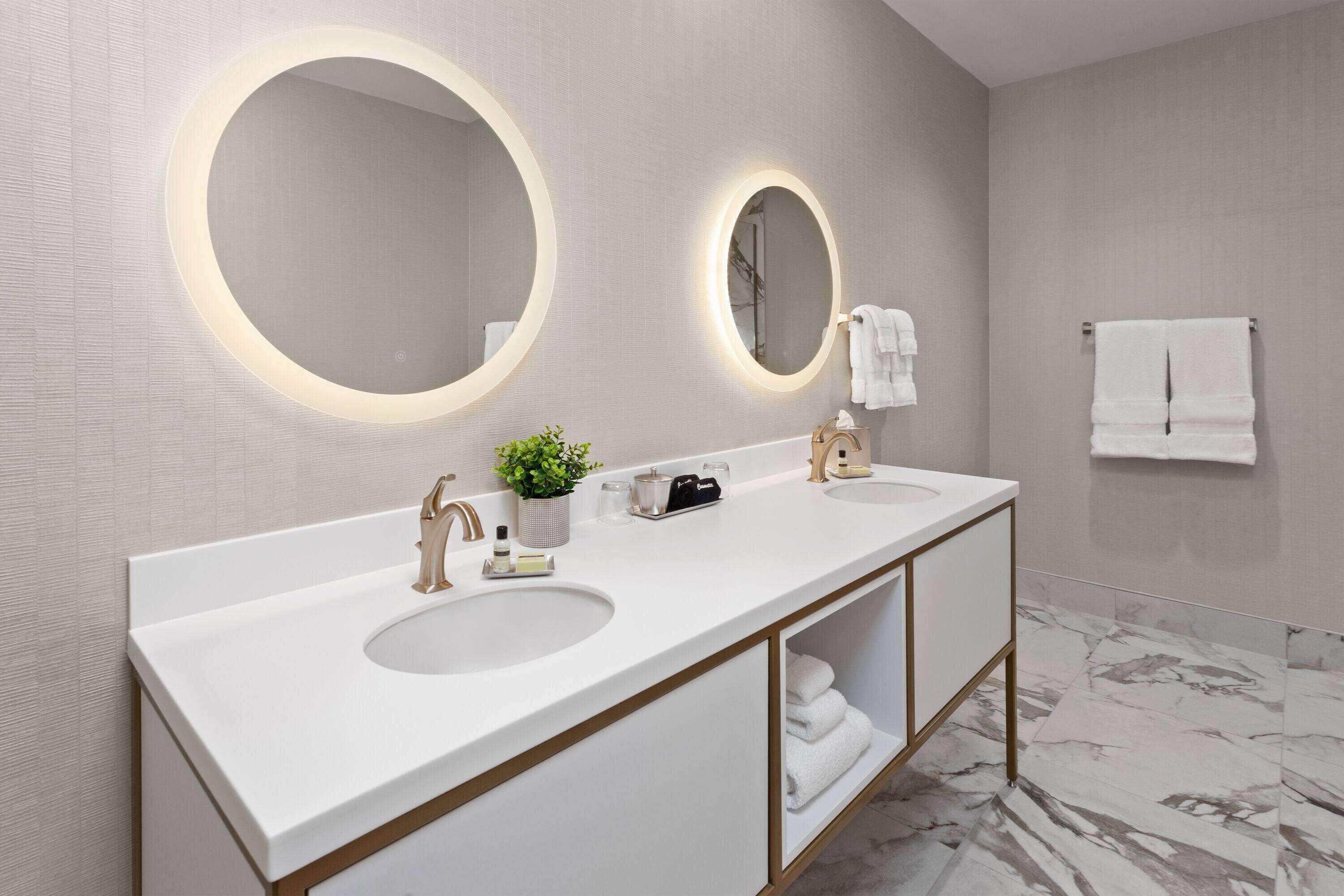 A modern bathroom with two sinks, a large mirror, and a marble floor.