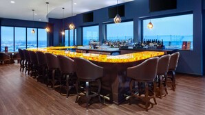 A bar area with a curved counter, multiple bar stools, and a view of the city through large windows. - Legacy Hotel Trademark Collection By Wyndham (Green Bay)