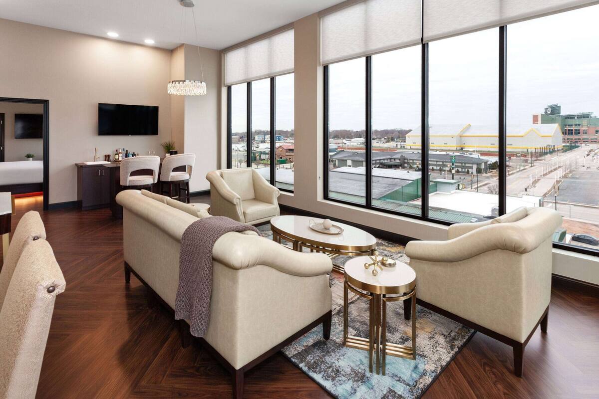Een moderne hotelkamer met een groot raam, een bank, twee fauteuils, een kleine tafel en een televisie.