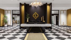 A lobby with a checkered floor, a reception desk, a chandelier, and a wall with a gold emblem. - Legacy Hotel Trademark Collection By Wyndham (Green Bay)