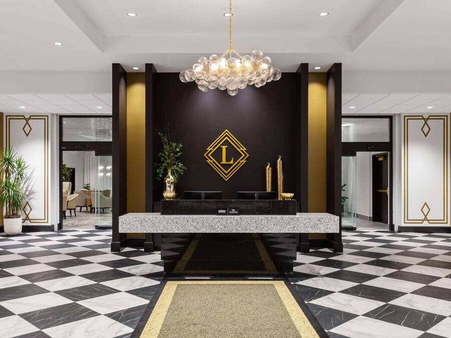 A lobby with a checkered floor, a reception desk, a chandelier, and a wall with a gold emblem.