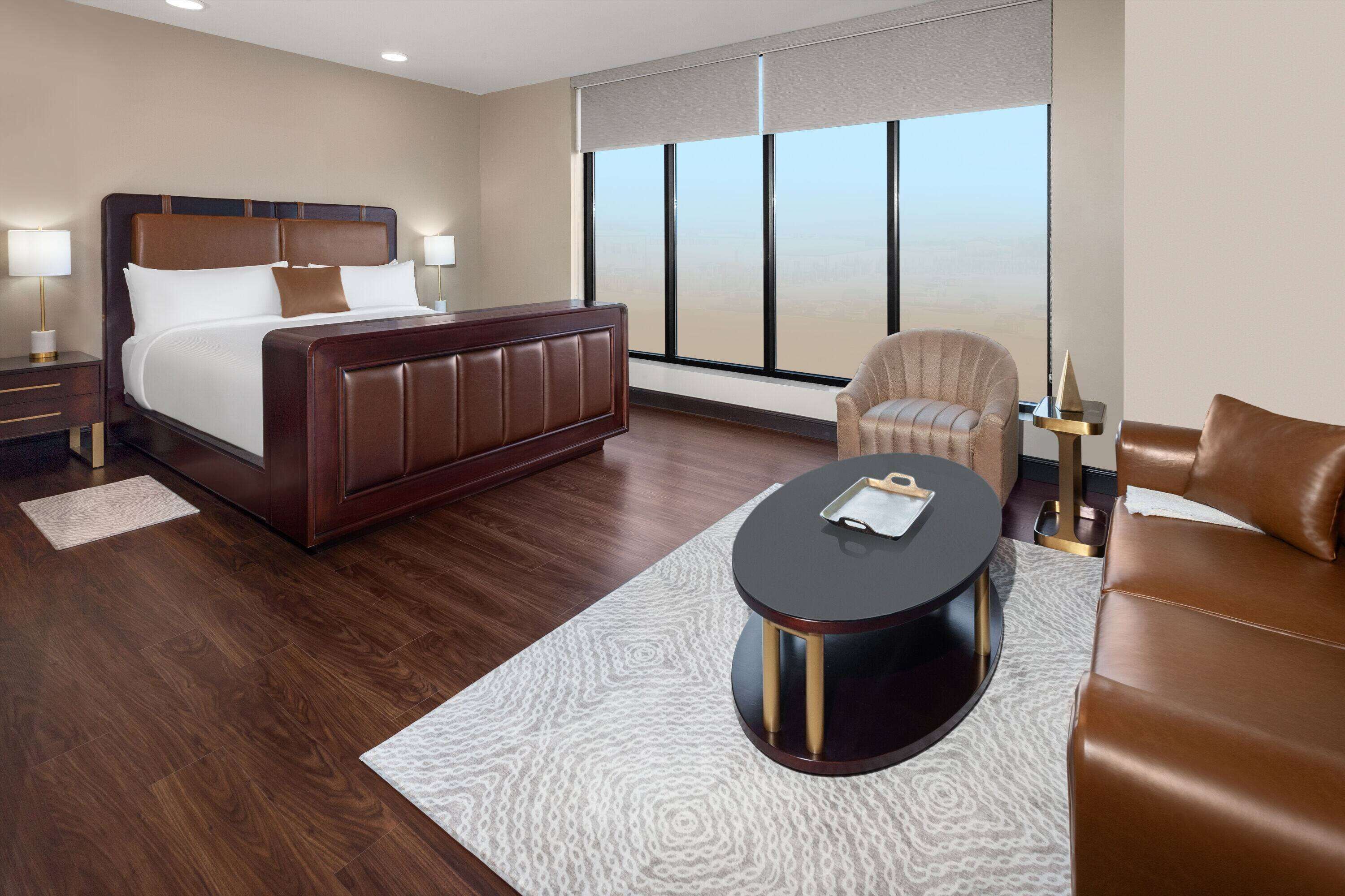 A hotel room with a large bed, a round coffee table, a sofa, and a chair.